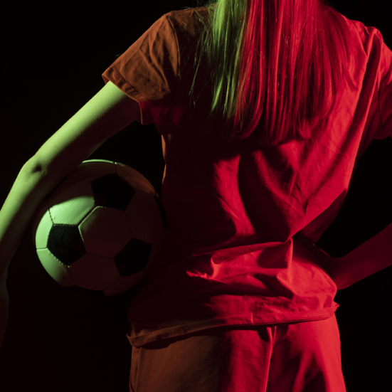 En kvindelig fodboldspiller med en bold under armen står med ryggen til.