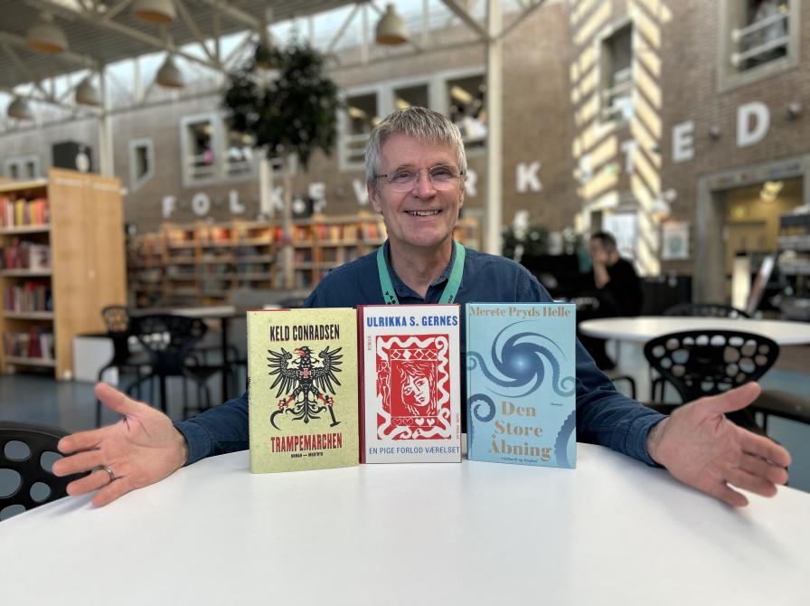 Erling sidder ved et hvidt bord på Hovedbiblioteket. På bordet har han sat alle tre romaner, som er omtalt i denne artikel, foran sig. De står alle med forsiderne frem og Erling laver en præsenterende gestus mod dem. Erling smiler og baggrunden, der viser biblioteksrummet med fyldte bogreoler, er let slørret.