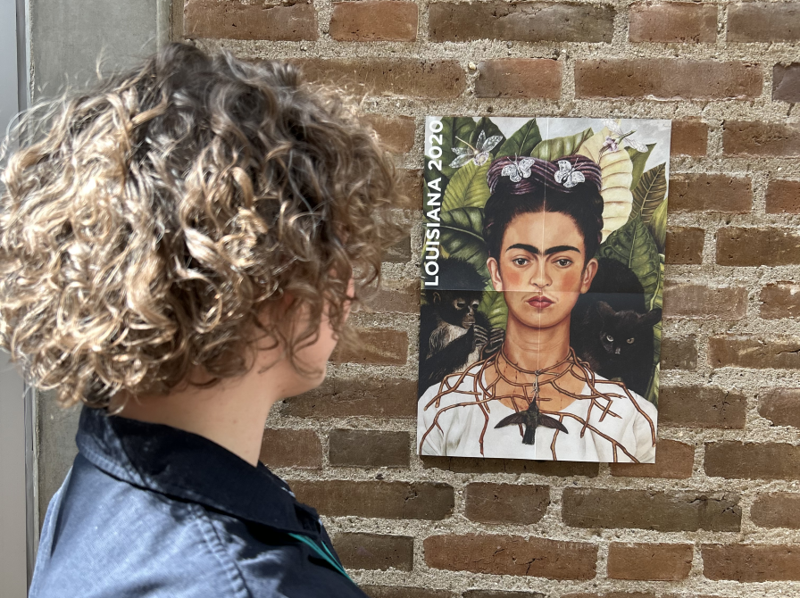 Ditte står og kigger på en plakat af et selvportræt af Frida Kahlo.